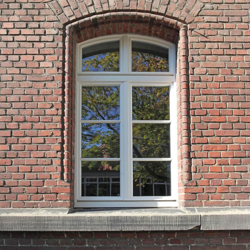Weißes Fenster mit Kreuzsprossen in einer roter Backsteinmauer
