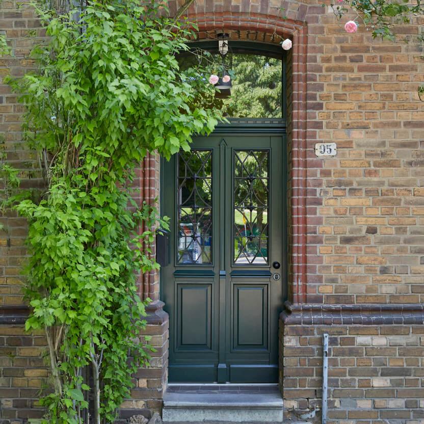 Dunkelgrüne Doppeltür mit Glasfenstern in einem roten Backsteinhaus