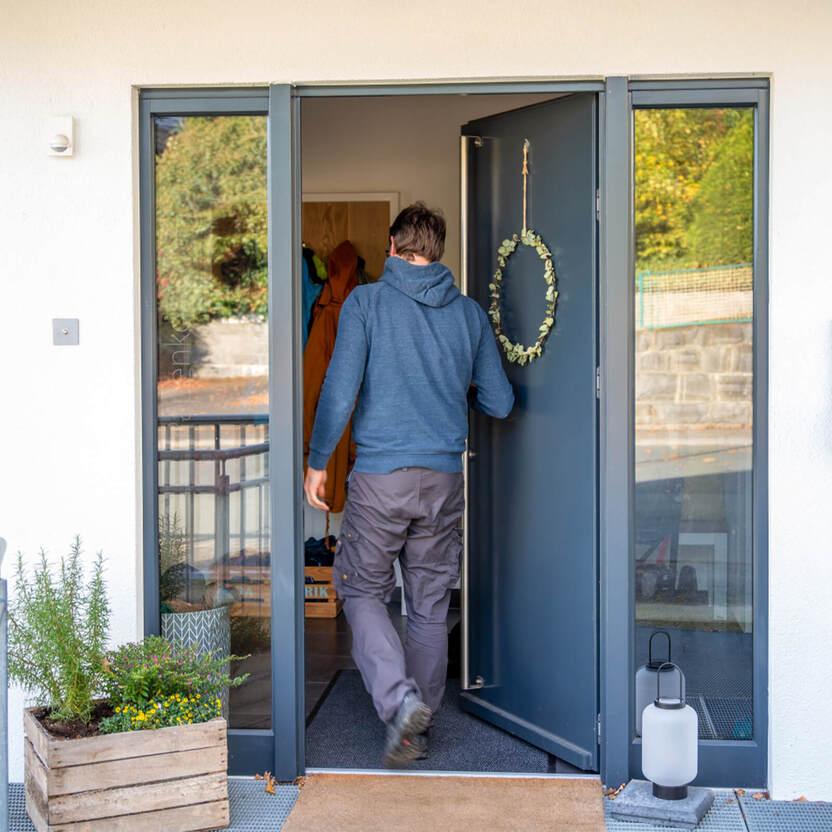Mann in blauem Kapuzenpullover betritt Haus durch offene blaue Haustür mit Türkranz