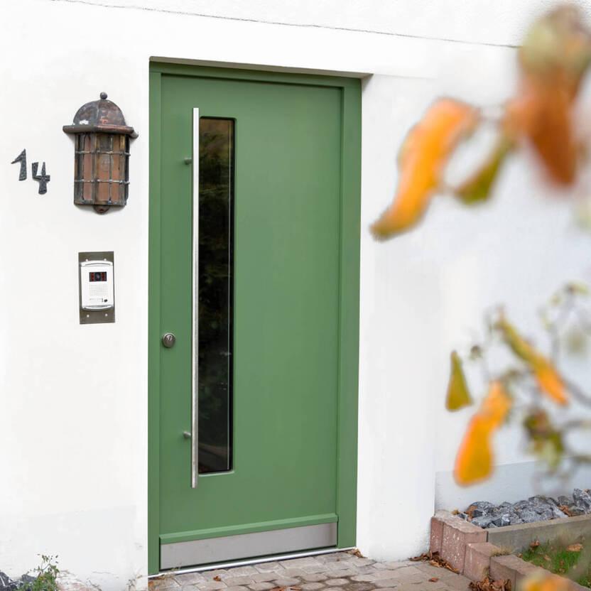 Grüne Haustür mit schmalem vertikalem Fenster und langem Griff