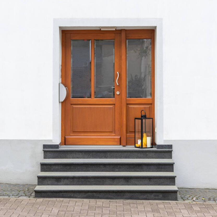 Holztür mit Glasfenstern und silbernem Griff, davor vier Stufen aus dunklem Stein