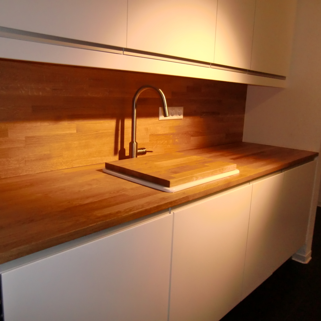 Detailansicht einer eleganten Küchenzeile mit weißer Schrankfront und einer Holzarbeitsplatte unter warmem Licht