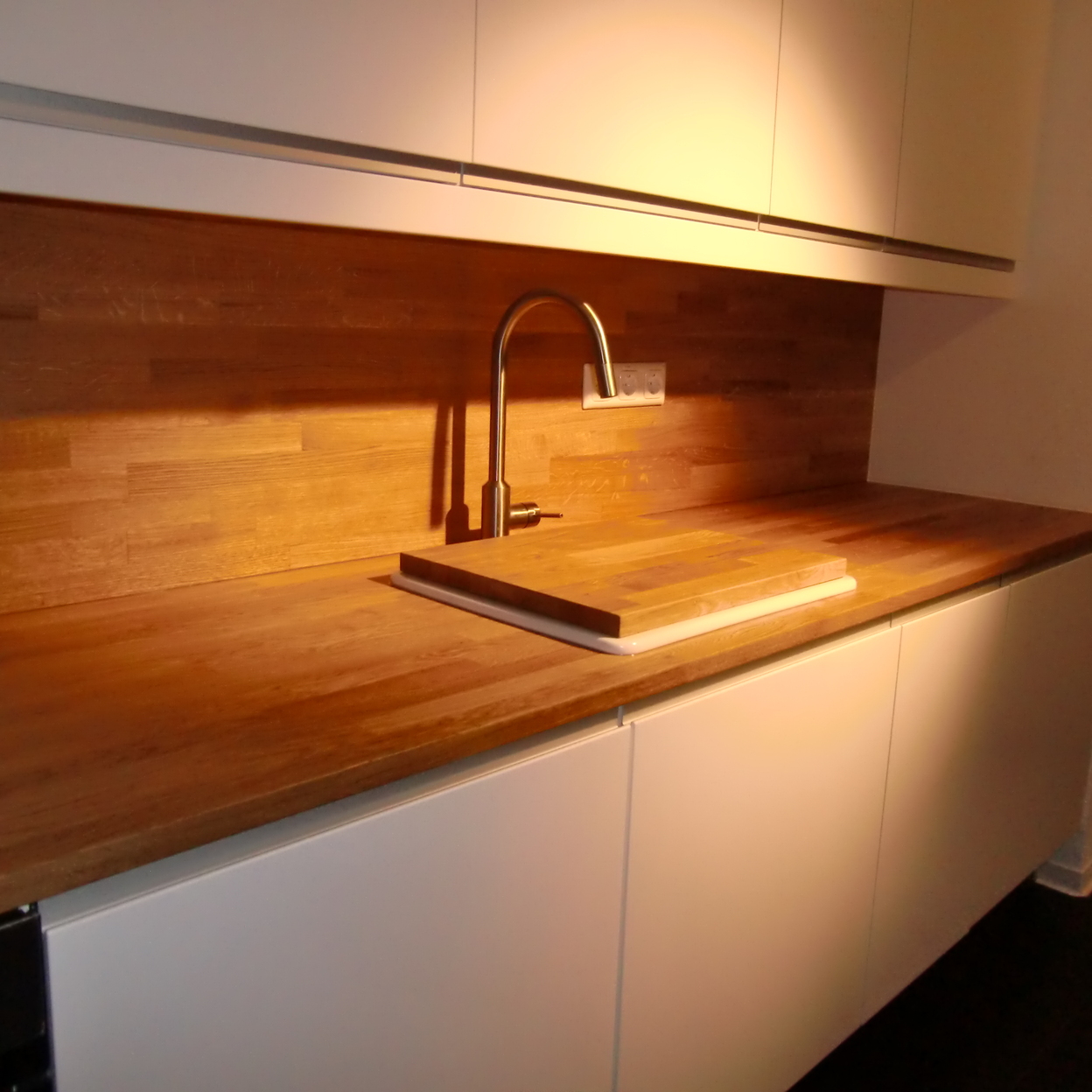Detailansicht einer eleganten Küchenzeile mit weißer Schrankfront und einer Holzarbeitsplatte unter warmem Licht