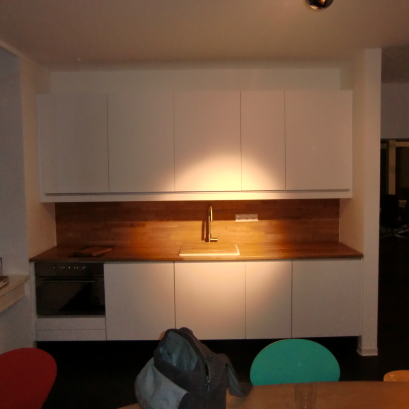 Abendansicht einer modernen Küche mit maßgefertigten weißen Schränken und einer warmen Holzarbeitsplatte, unterstrichen durch sanfte Beleuchtung. Ideal für Küchen nach Maß.