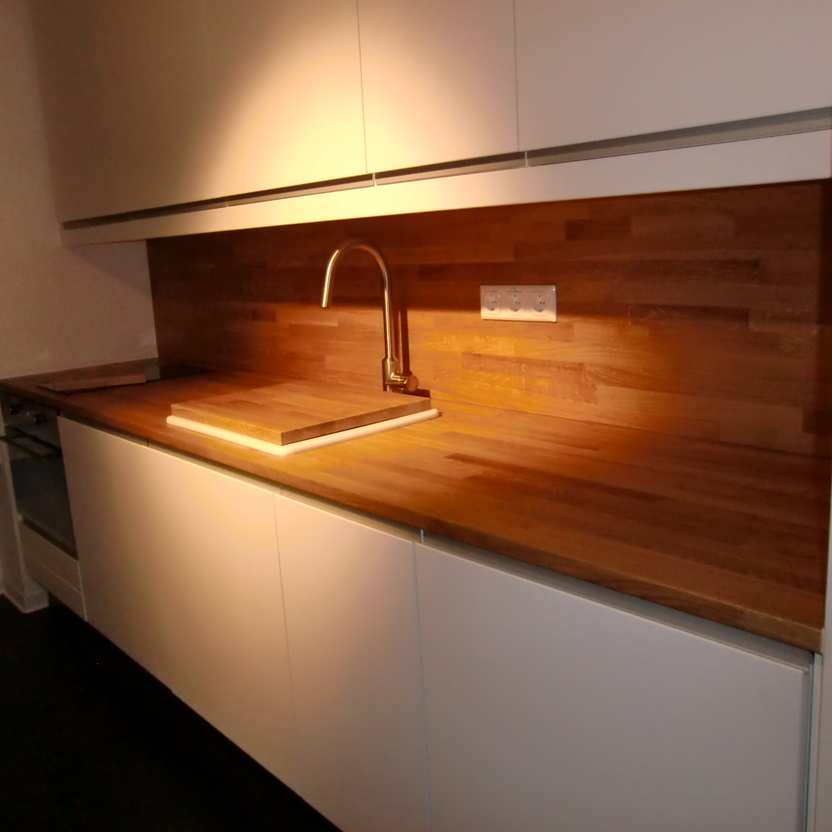 Nahaufnahme einer maßgefertigten Küche mit modernen weißen Schränken und einer Holzarbeitsplatte, beleuchtet durch ein warmes Licht.