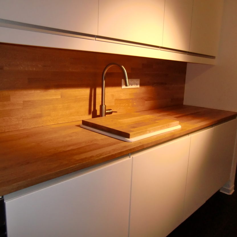 Detailansicht einer eleganten Küchenzeile mit weißer Schrankfront und einer Holzarbeitsplatte unter warmem Licht