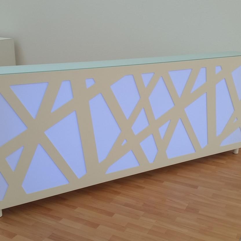 Moderner Empfangstresen mit Beleuchtung Weißer Empfangstresen mit geometrischem Muster und hinterleuchteter blauer Oberfläche, aufgestellt in einem Raum mit hellem Laminatboden.