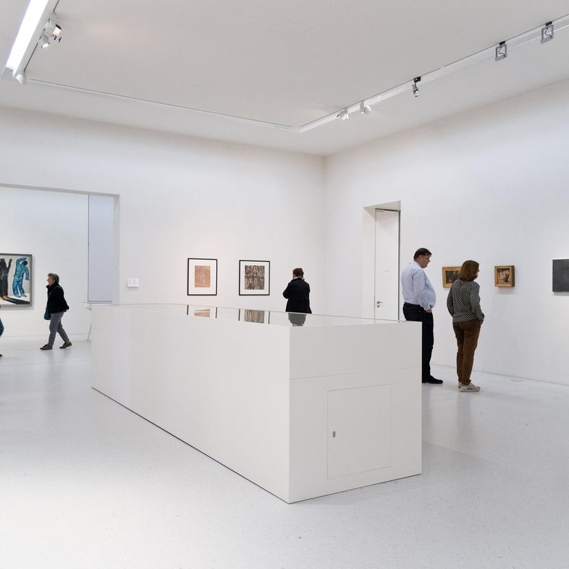 Besucher in einer Kunstgalerie betrachten Kunstwerke, umgeben von minimalistischem Vitrinenbau, der die Räumlichkeiten strukturiert.