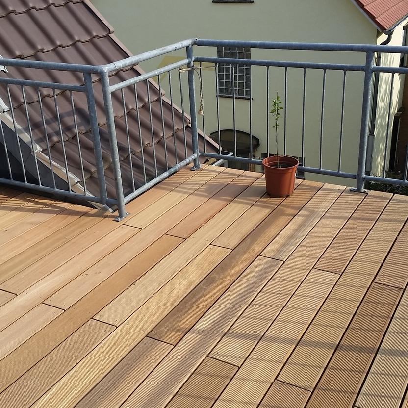 Moderne Holzterrasse mit Geländer Eine Holzterrasse mit hellen Dielen und einem Metallgeländer, im Hintergrund Dachflächen und Häuser. Ein einzelner Blumentopf steht in der Ecke. Keyword: Holzterrasse.