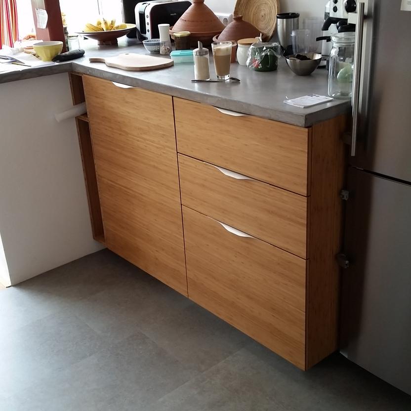 Maßgefertigte Küche mit Schränken aus Holzfronten, Betonarbeitsplatte und modernem Kühlschrank, ergänzt durch Küchenutensilien und eine helle Raumgestaltung.