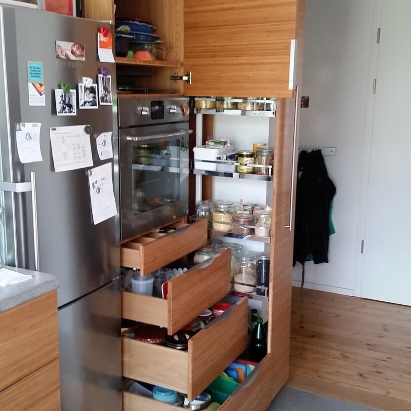 Geöffneter Küchenhochschrank mit Schubladenauszügen, Vorratsgläsern und eingebautem Backofen