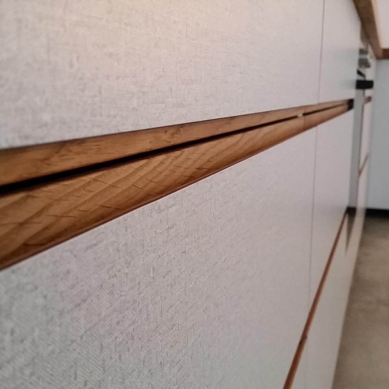 Detailansicht griffloser Küchenschubladen mit Holzgriffleiste und Strukturfront Nahaufnahme strukturierter Küchenschubladen mit eingelassener Holzgriffleiste in moderner Küche