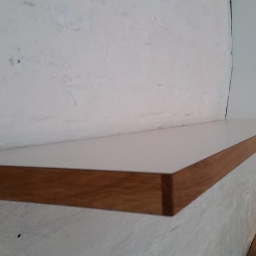 Nahaufnahme eines minimalistischen Wandregals mit weißer Oberfläche und Holzkante in Küche