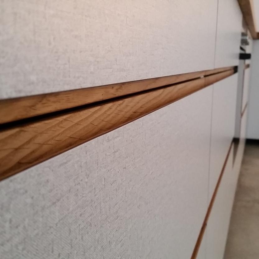 Nahaufnahme strukturierter Küchenschubladen mit eingelassener Holzgriffleiste in moderner Küche