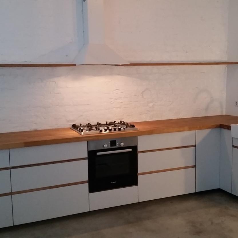 Moderne, weiße L-Küche mit Holzplatte, Gasherd, Backofen, Spüle und Wandregal