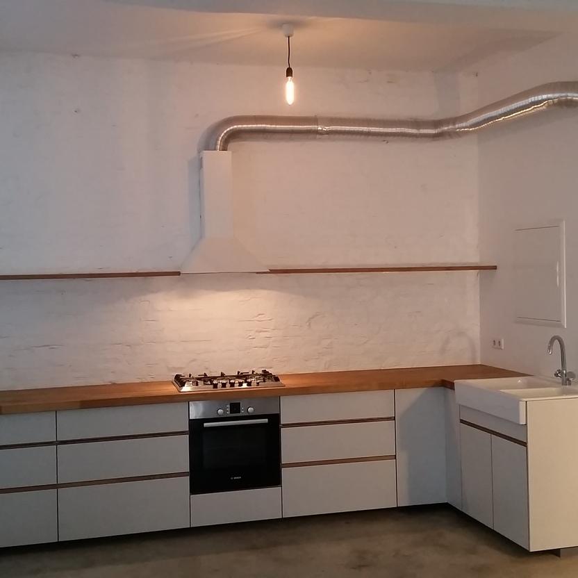 Moderne, weiße L-Küche mit Holzplatte, Gasherd, Backofen, Spüle und Wandregal