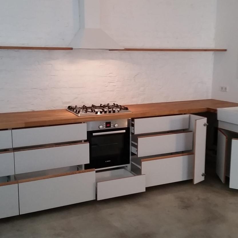 Moderne, minimalistische Küche mit weißen Fronten, offener Holzarbeitsplatte, eingebautem Gasherd und Backofen, einem Wandregal und Doppelspüle. Die Wand ist aus weiß gestrichenem Backstein.