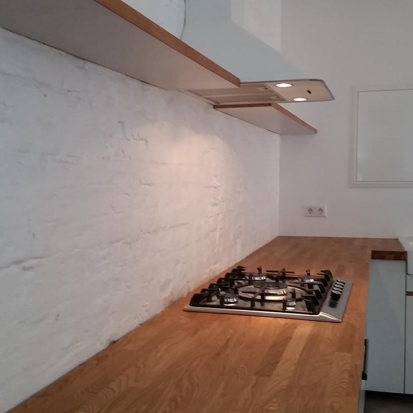 Moderne Küchenzeile mit Gasherd, weißer Spüle, Holzarbeitsplatte und schwebendem Regal