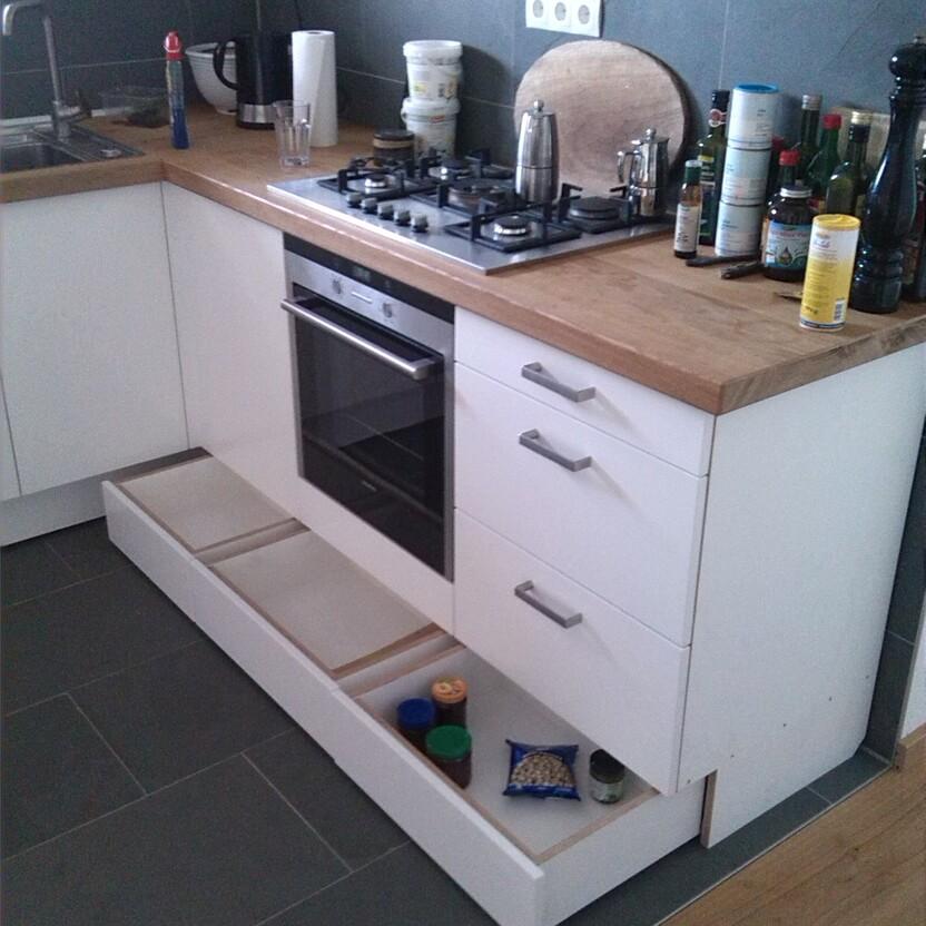 Weiße Küche mit geöffneten Sockelschubladen unter dem Herd zur Aufbewahrung von Vorräten