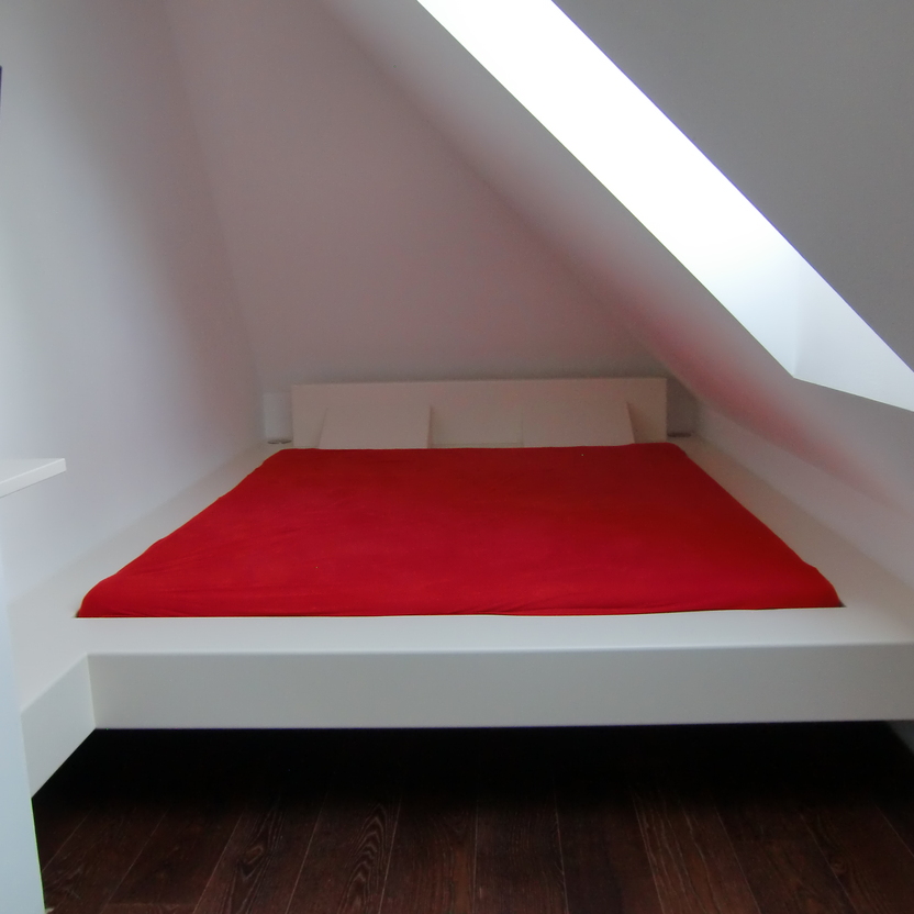 Ein modernes, unter einer Dachschräge eingebautes Bett in einem minimalistischen Raum, illustriert präzisen Möbelbau mit einer leuchtend roten Bettdecke.