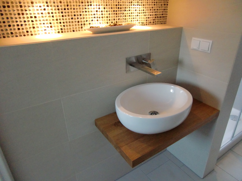 Moderne Waschschale auf einer maßgefertigten Holzplatte, montiert an einer gefliesten Wand mit einem dekorativen Mosaik als Hintergrund.