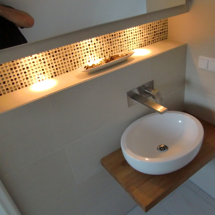 Modernes Waschbecken auf einem Holzbrett, eingebettet in eine Wandnische mit dekorativer Mosaikbeleuchtung. Ein Beispiel für ein individuell gestaltetes Bad nach Maß.