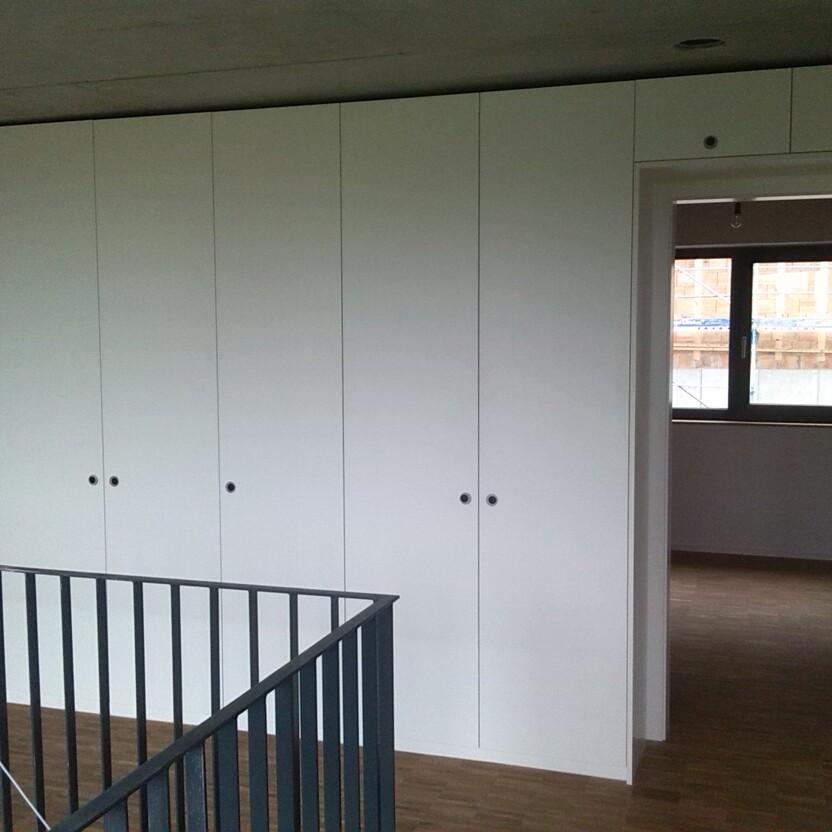 Großer weißer Wandschrank in einem modernen Raum Eine Wand aus großen, weißen Schränken in einem hellen Raum mit Holzboden, bietet umfangreichen Stauraum und eine schlichte Ästhetik.