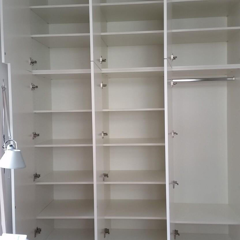 Großes weißes Einbauregal in einem Zimmer Ein großes, offenes, weißes Einbauregal mit mehreren Fächern auf Holzboden in einem hellen Raum, ideal zur Aufbewahrung und Präsentation.