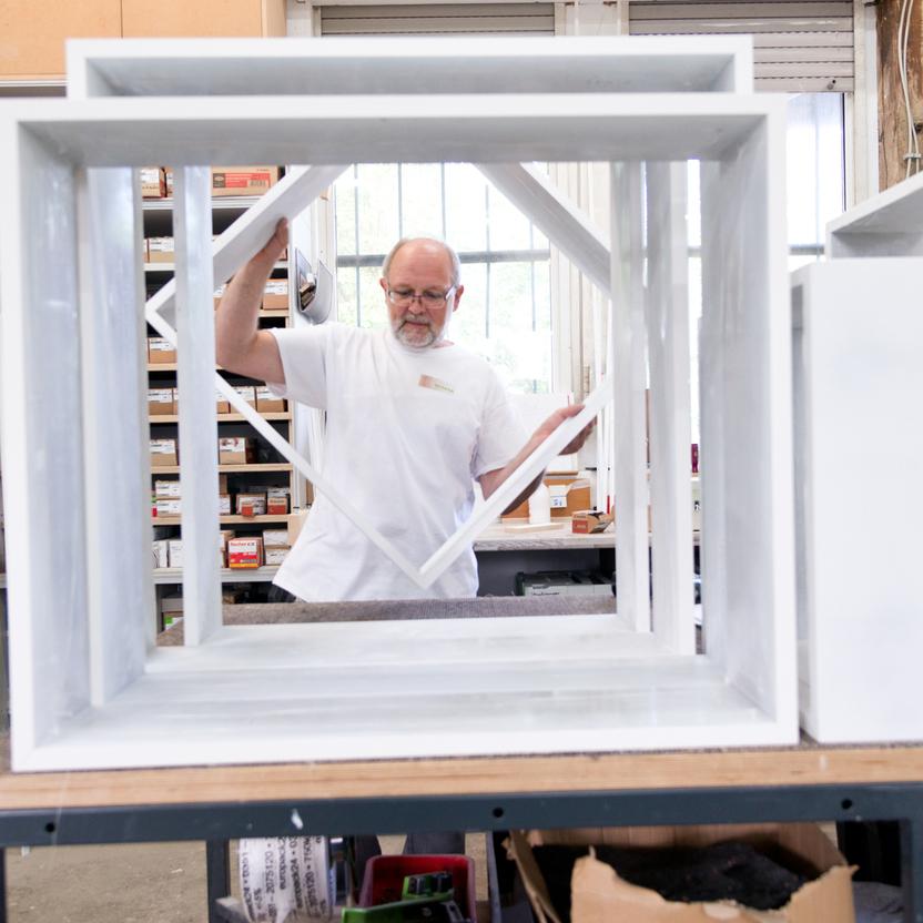 Ein Handwerker inspiziert sorgfältig ein frisch lackiertes Möbelstück in einer gut ausgestatteten Werkstatt.