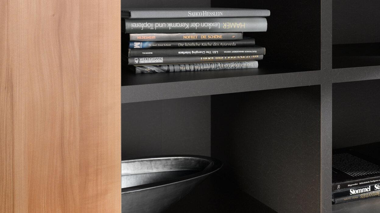 Detailaufnahme eines schwarz lackierten Regals mit B&uuml;chern und Schale in Kombination mit naturbelassenem Holz.